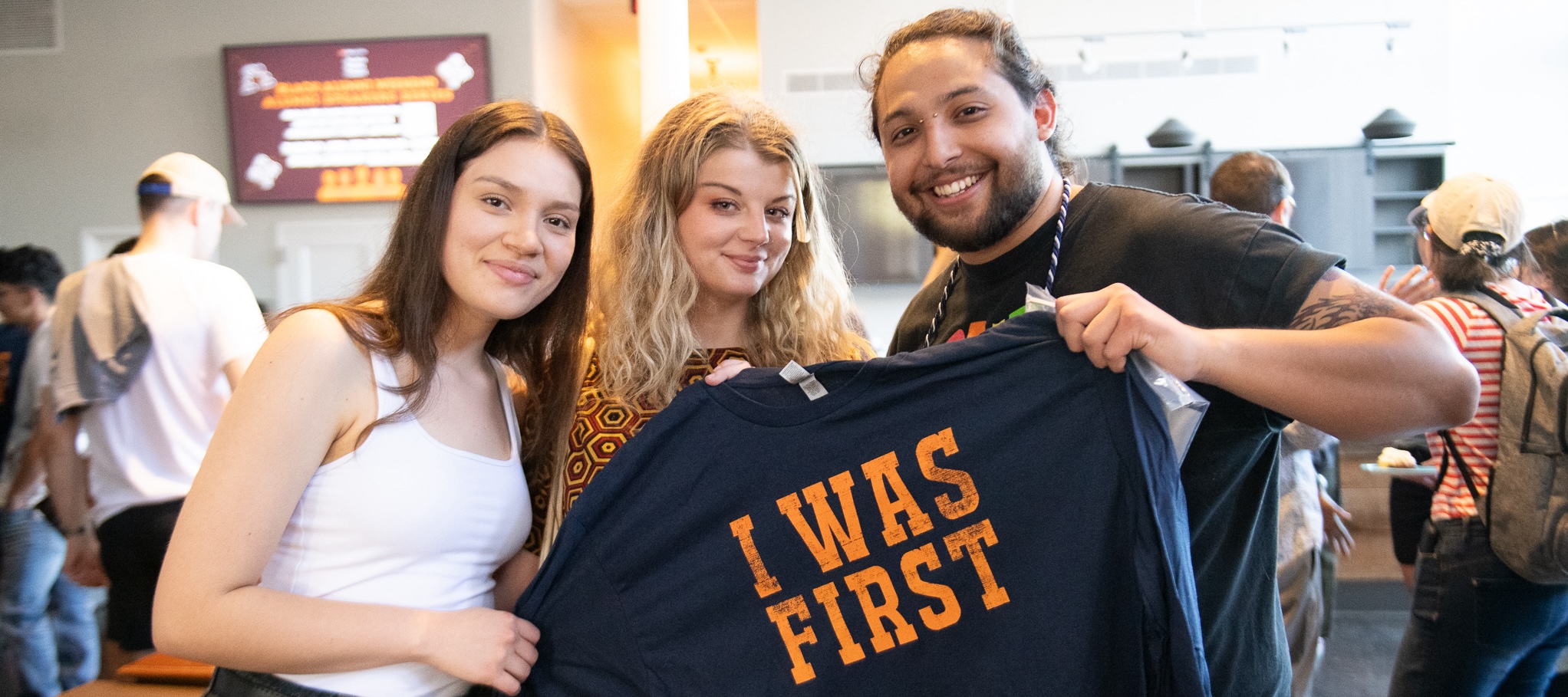 Three students holding up "I Was First" shirt